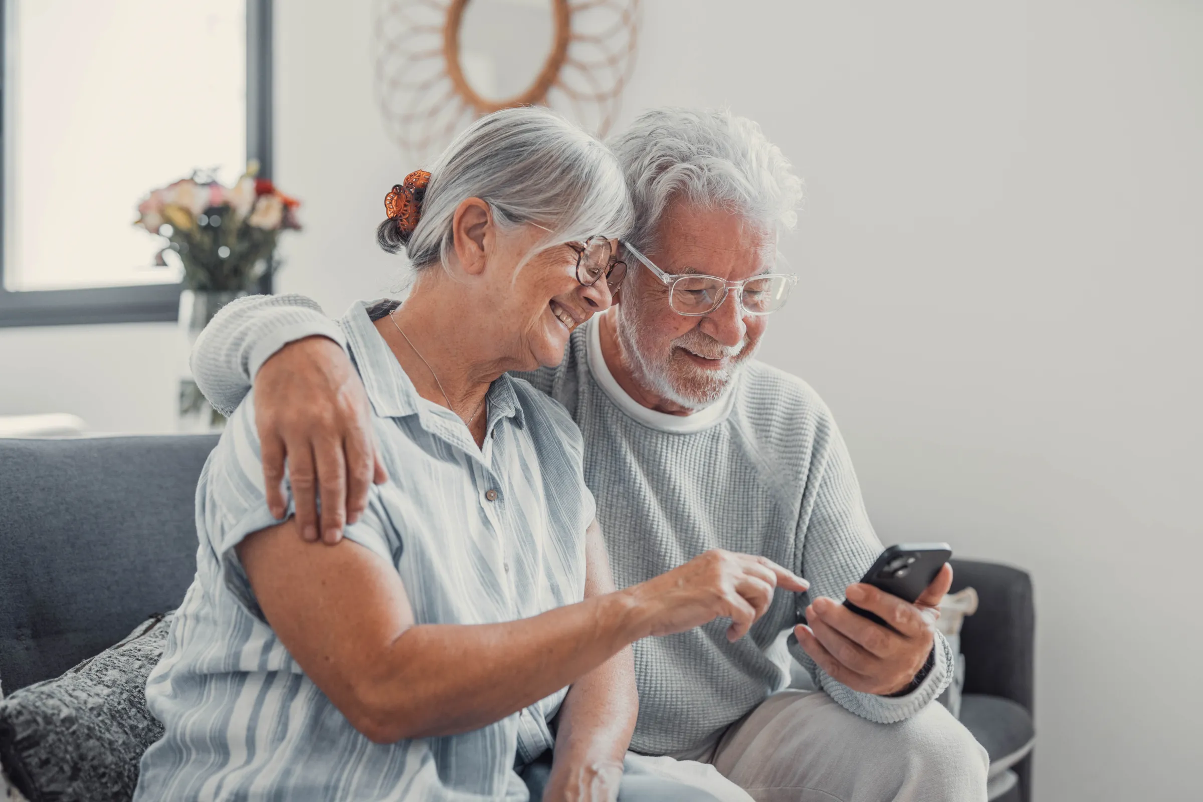 Senior couple, phone and relax on sofa for hug, choice and help with video, download and streaming in home. Elderly woman, man and smartphone on couch in lounge with thinking for post on social media